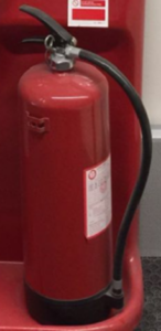 Extintor de polvo ABC de color rojo cargado y preparado colocado sobre una base disponible en caso de incendio