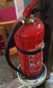 Extintor de polvo ABC de color rojo cargado y preparado colocado sobre una base disponible en caso de incendio